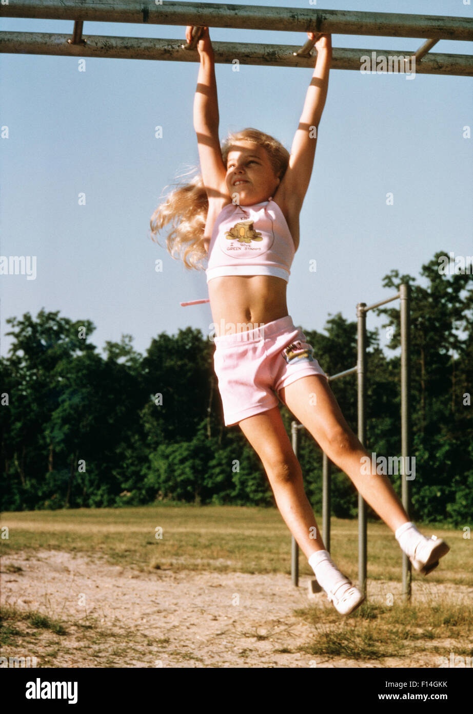 1970ER JAHRE MÄDCHEN HÄNGEN VOM KLETTERGERÜST IN SPIELPLATZ TRAGEN ROSA BIKINI-TOP UND SHORTS Stockfoto