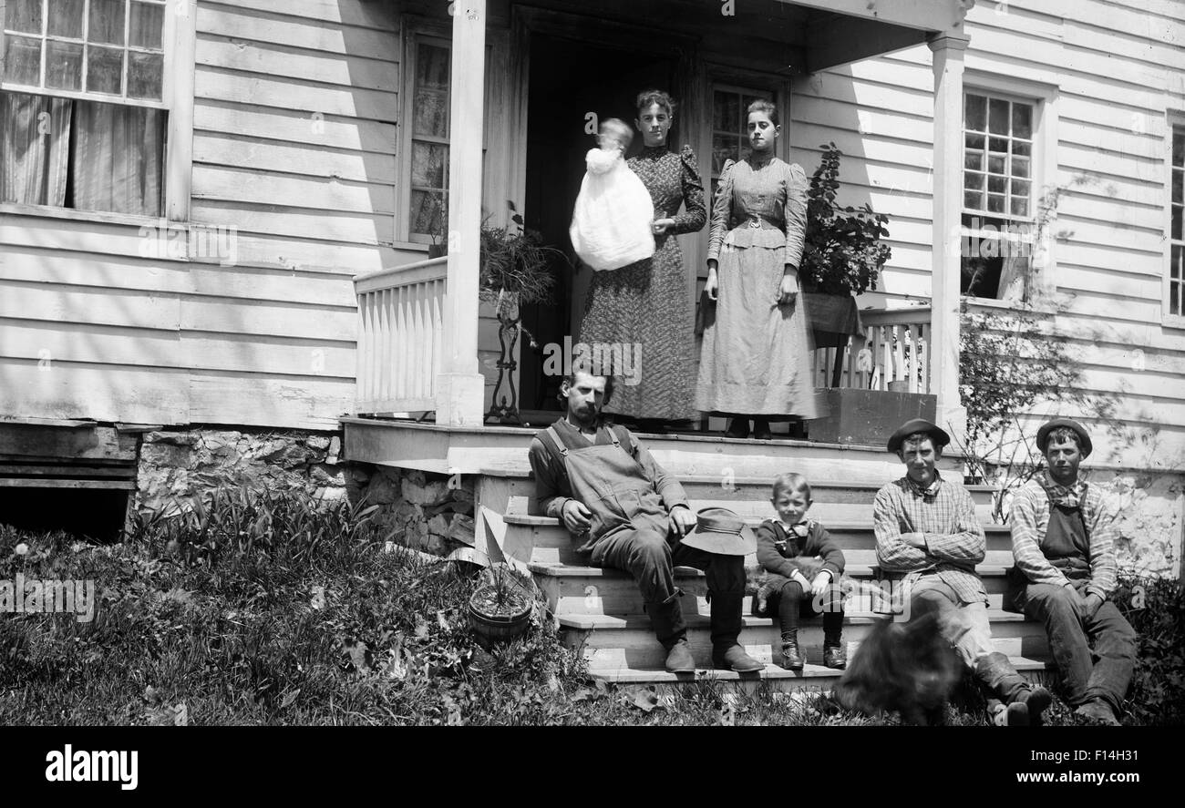 1890ER JAHRE GRUPPE PORTRAIT FAMILIE ERWACHSENE KINDER SITZEN STEHEN AUF DER VERANDA DES HAUSES, BLICK IN DIE KAMERA ZU POSIEREN Stockfoto