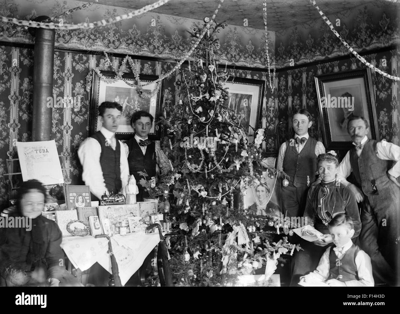 1890 1890S WENDE DES JAHRHUNDERTS GRUPPE PORTRAIT FAMILIE DREI GENERATIONEN POSING BY WEIHNACHTSBAUM GESCHENKE AUF TISCH Stockfoto