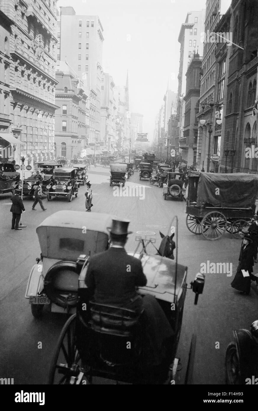 1910ER JAHRE 5TH AVE BEI 43. AUSSEHENDE NORTH CARS WAGEN FUßGÄNGER EIN HANSOM CAB UND FAHRER IM OBEREN HUT IM VORDERGRUND NEW YORK CITY USA Stockfoto