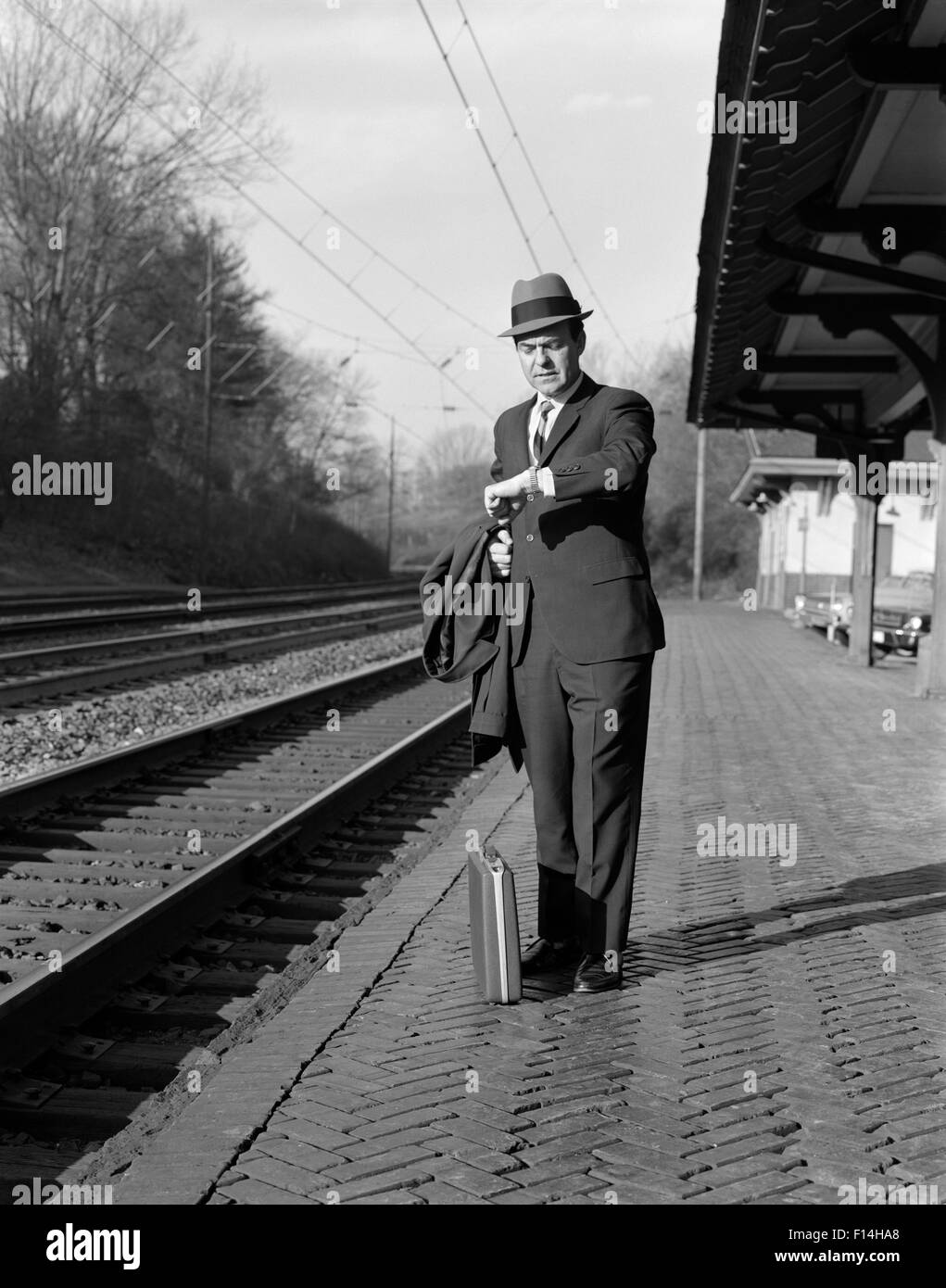 1960ER JAHRE MANN PENDLER GESCHÄFTSMANN WARTEN AUF ZUG BLICK AUF ZEIT ARMBANDUHR Stockfoto