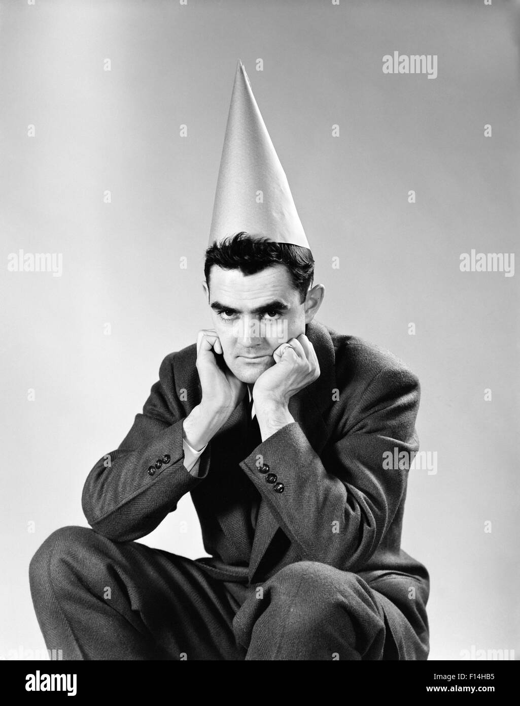 1950ER JAHRE DISGUNTLED MANN TRÄGT DUNCE CAP BLICK IN DIE KAMERA Stockfoto
