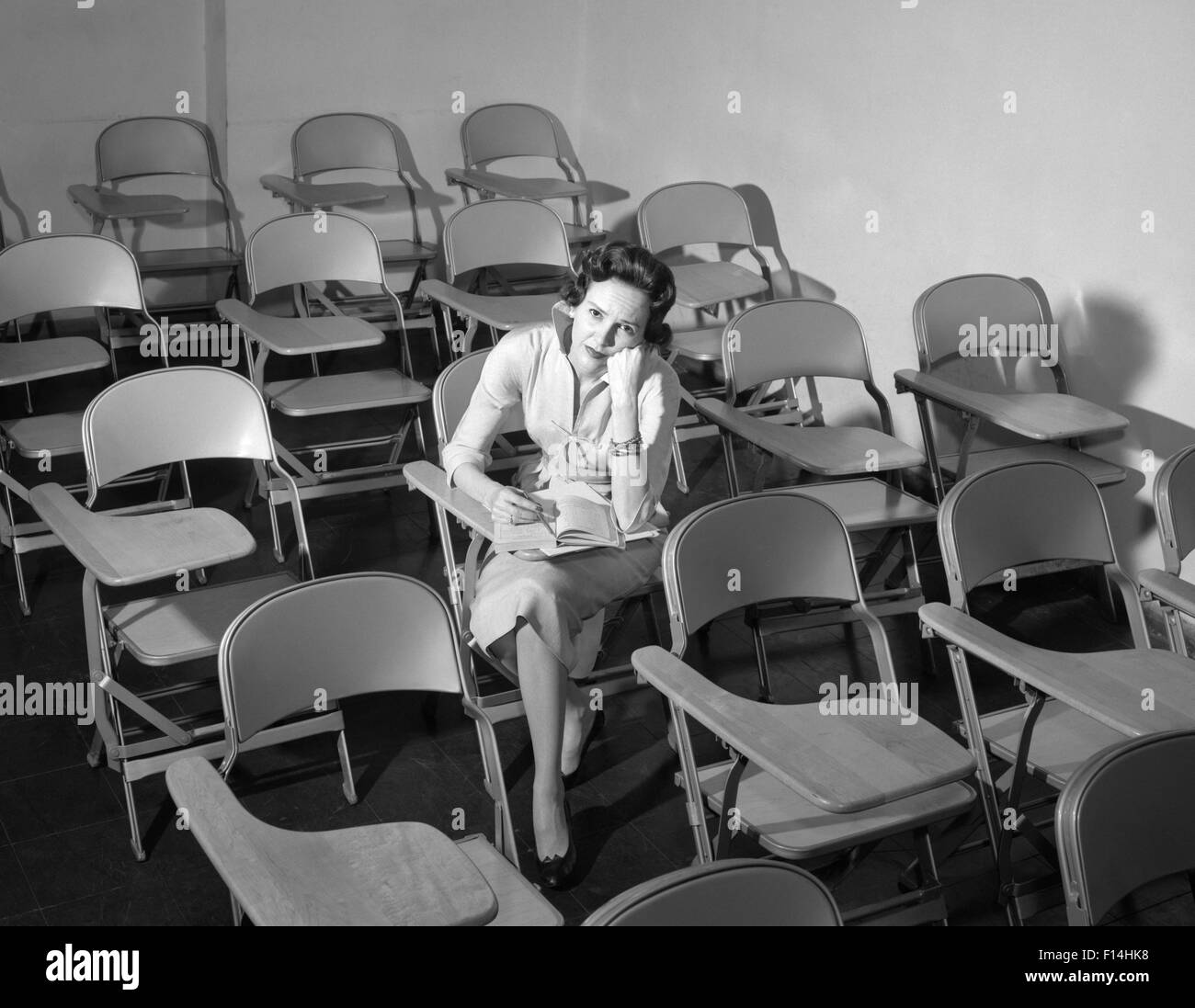 1950ER JAHREN FRAU SITZT IM KLASSENZIMMER LEEREN STÜHLE VERÄRGERT Stockfoto