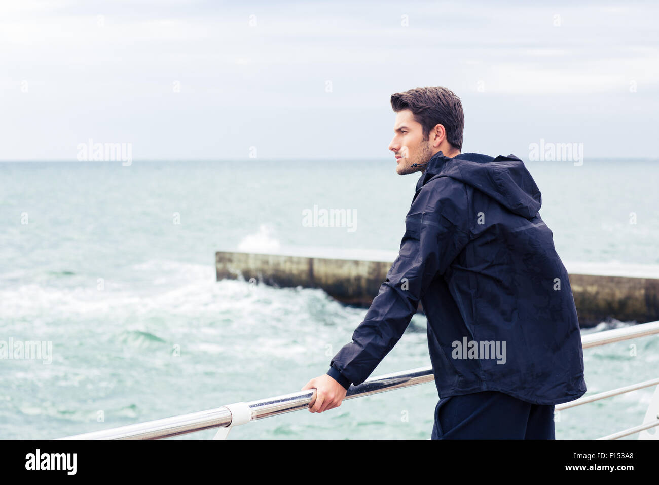 Junger Mann in Sportbekleidung steht in der Nähe von Meer im freien Stockfoto