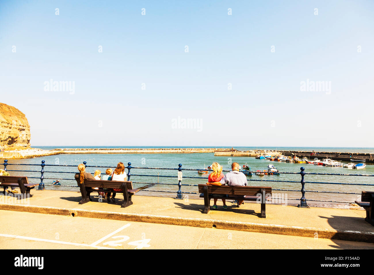 Menschen saßen auf Bänken Bank Blick auf das Meer Küste Küste Staithes Dorf Hafen Bucht Mündung Hafenstadt UK England Stockfoto