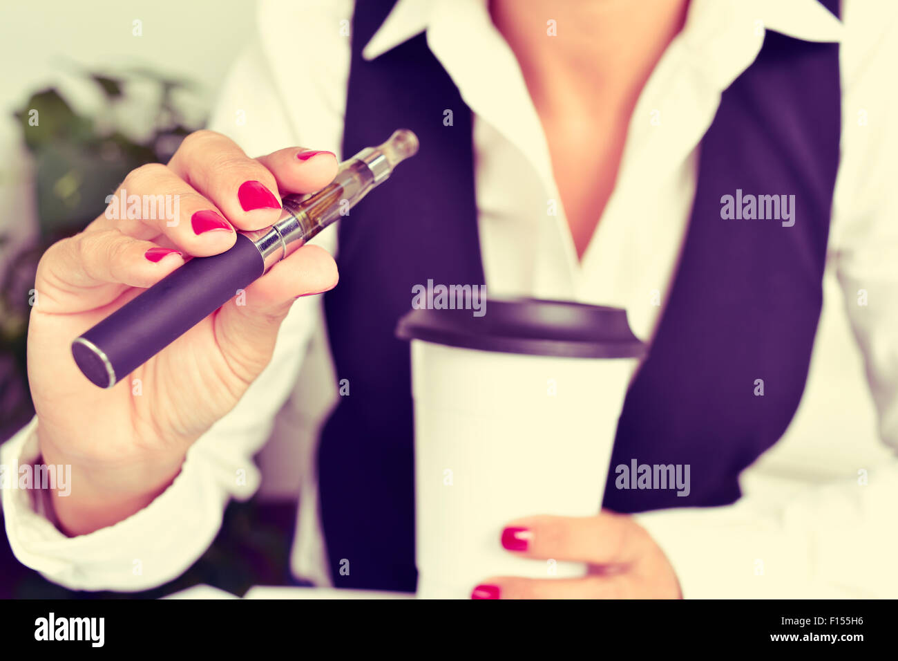 eine junge kaukasischen Frau, mit einer Tasse Kaffee in der Hand, dampft aus einer elektronischen Zigarette Stockfoto