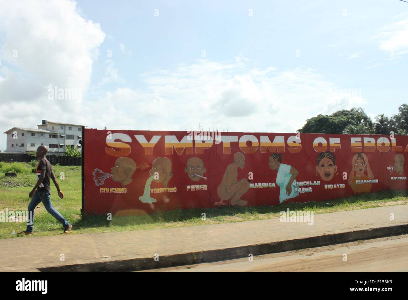 Ein liberianischer Mann geht vorbei an einer öffentlich-rechtlichen Plakatwand Auflistung der Symptome von Ebola Bestandteil einer öffentlichen Bildung Outreach zur Eindämmung des Ausbruchs 23. Dezember 2014 in Monrovia, Liberia. Stockfoto