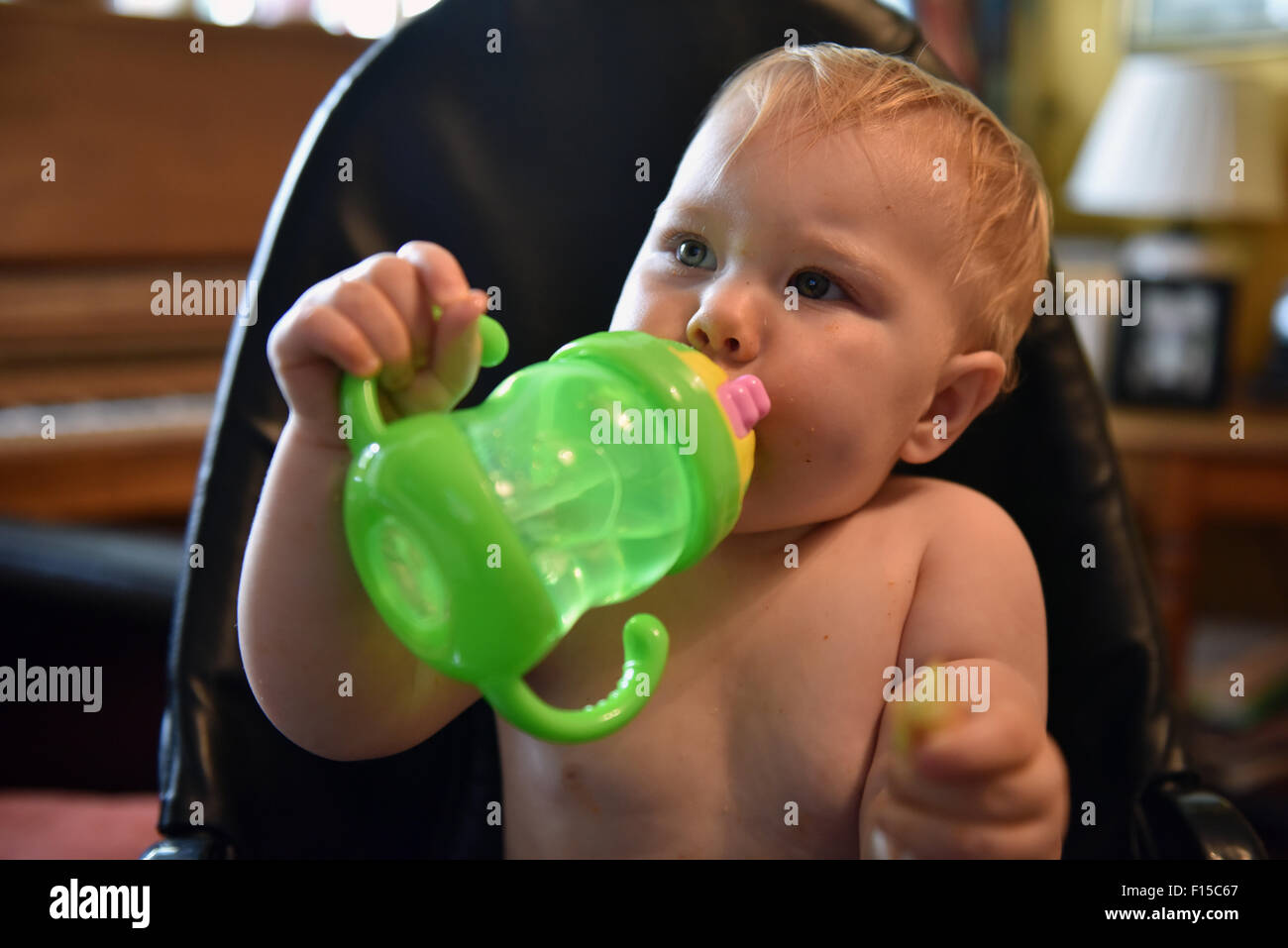 Ein elf Monate altes Baby sitzen in ihrem Hochstuhl Trinkwasser aus einem hellen grünen Becher. Stockfoto