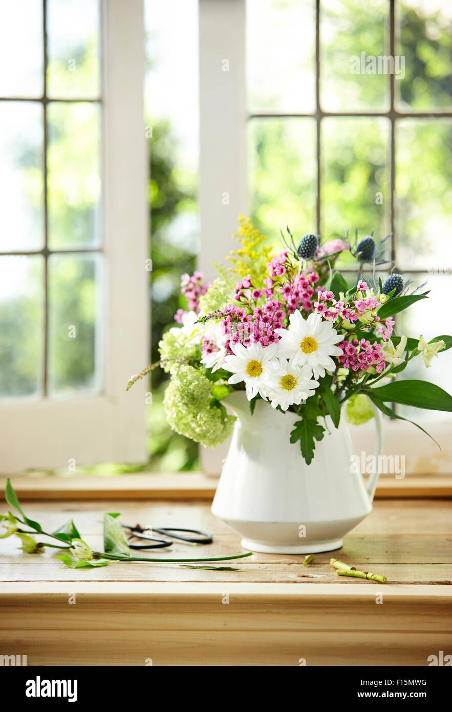 Bouquet von frischen Schnittblumen mit Daisy, Flox, Meer Holly, Hortensie und Ambrosia in weiß Krug Vase auf Fensterbank Stockfoto