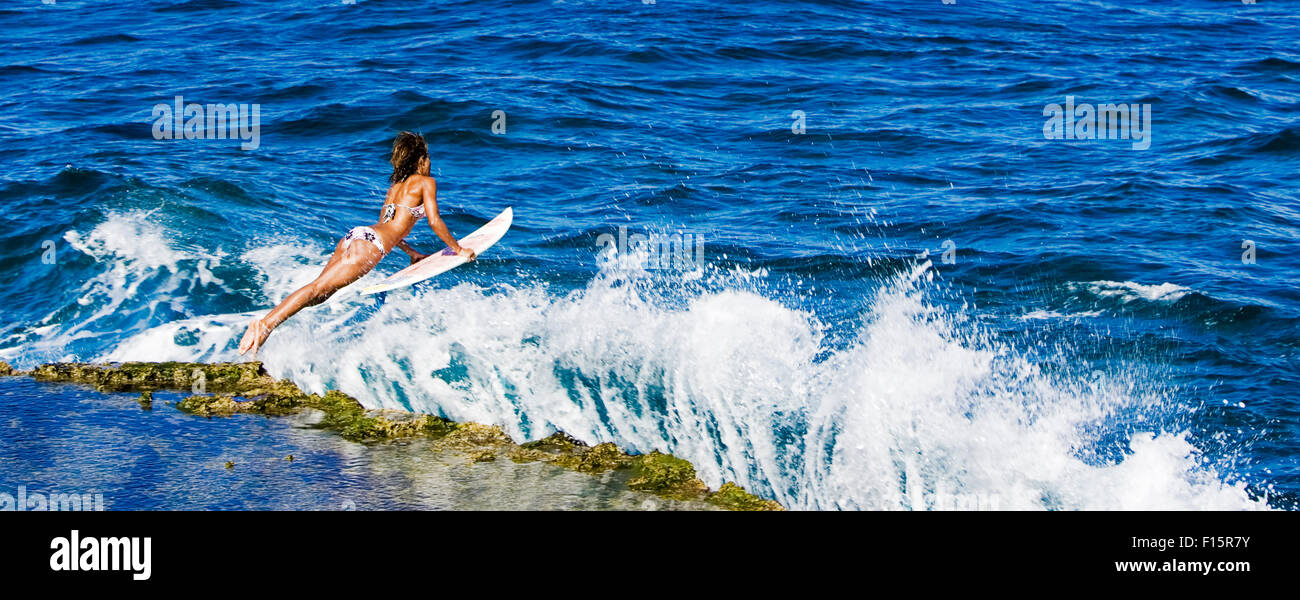 dramatische Aktion Bildniss Surferin startet aus Felsen mit Surfbrett über Wellen in Ozean Stockfoto