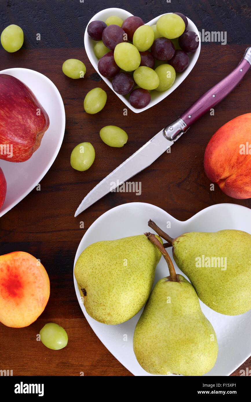 Auswahl an Obst, wie Äpfel, Birnen, Nektarinen und Trauben auf weißes Herz Form Platten auf rustikalen Holztisch, overhead. Stockfoto