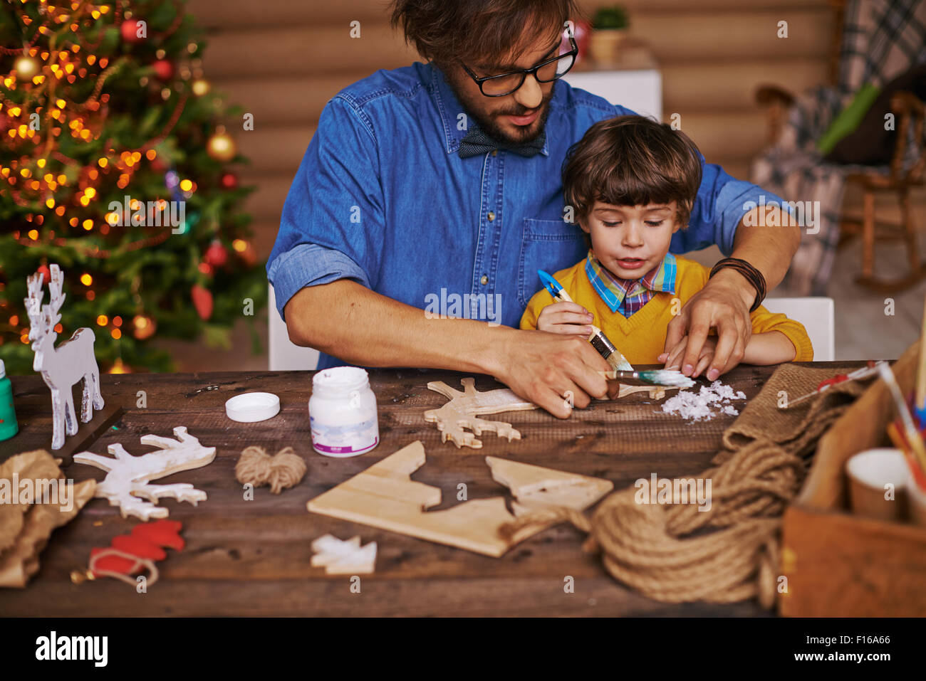Junger Mann zeigt seinen kleinen Sohn wie Xmas Holzspielzeug zu malen Stockfoto