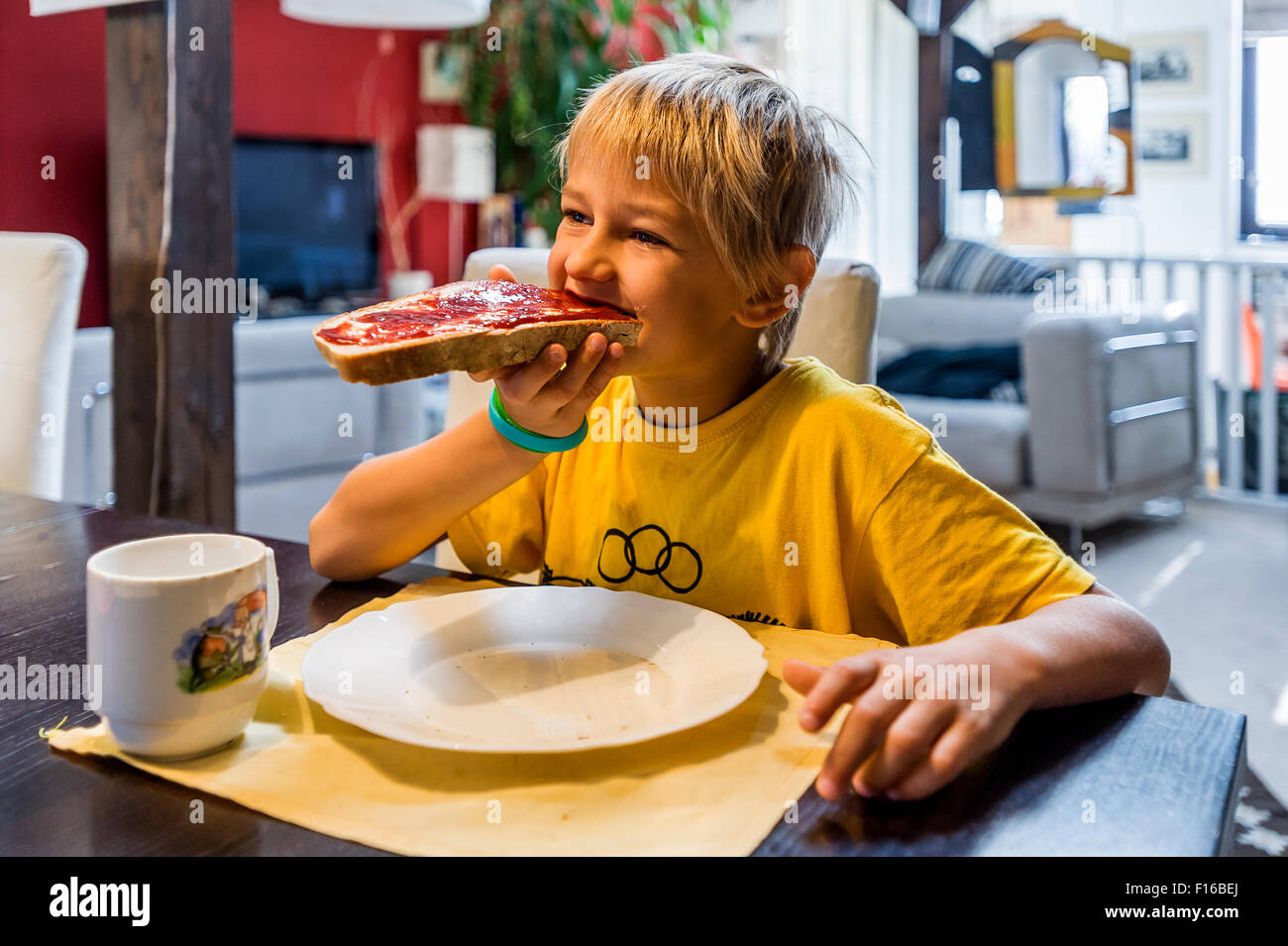 Blondschopf im gelben Trikot Essen an den Tisch Brot und Marmelade Stockfoto