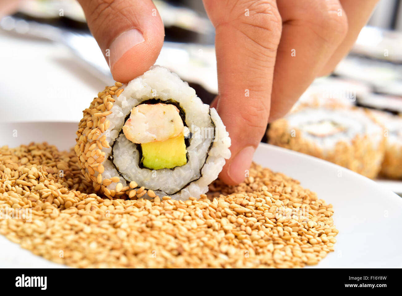 Nahaufnahme eines jungen Mannes Vorbereitung Uramaki, gefüllt mit Avocado und Garnelen und garniert mit Sesam Stockfoto