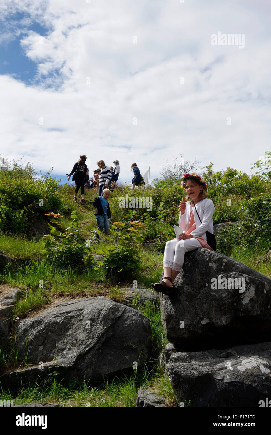 Mädchen trägt Kranz und sitzt auf einem Felsen, während die Kinder spielen am Hang. Stockfoto