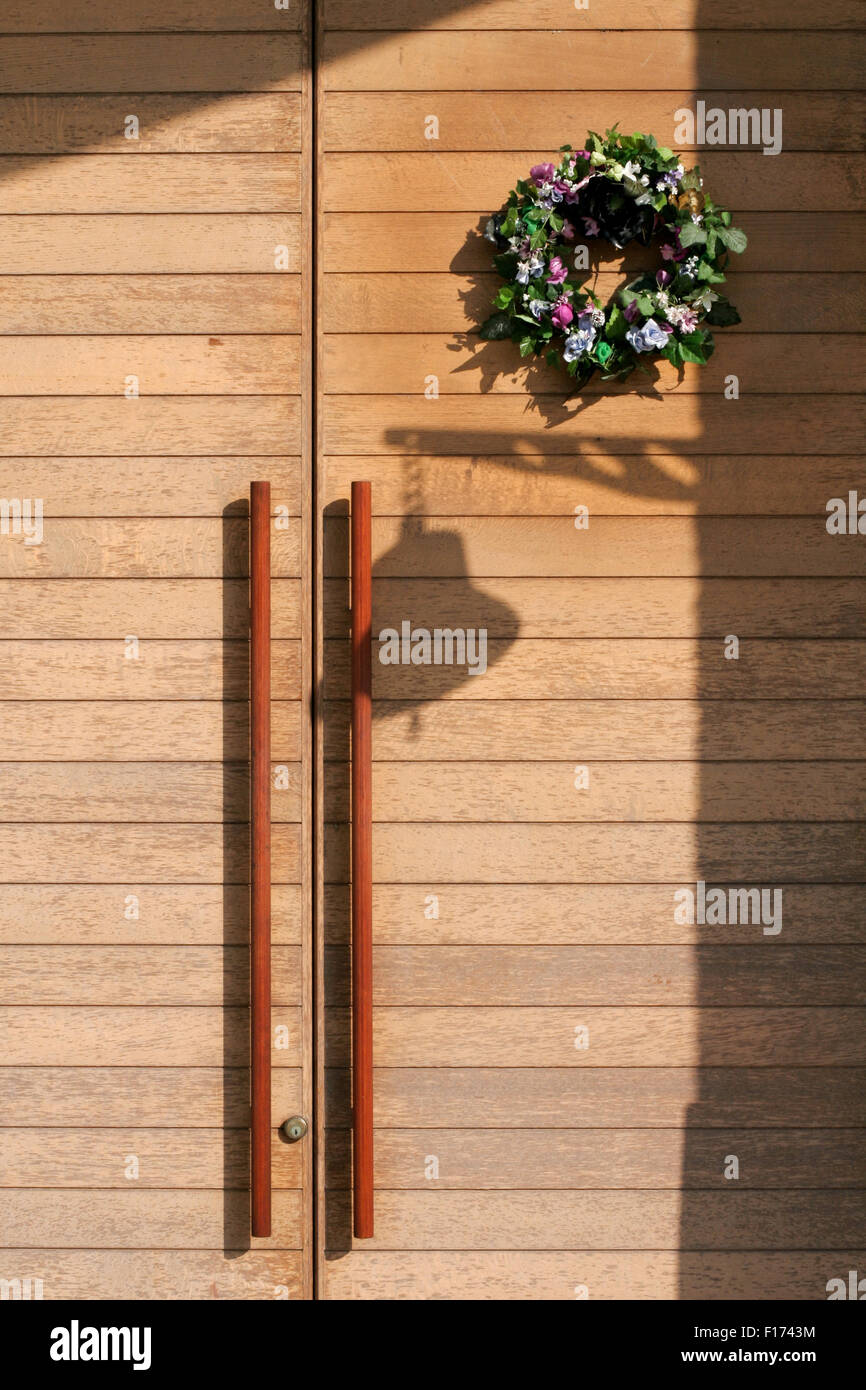 Haustür aus Holz klare Linien Glocke Silhouette und Blumenkranz mittlere Sicht Stockfoto