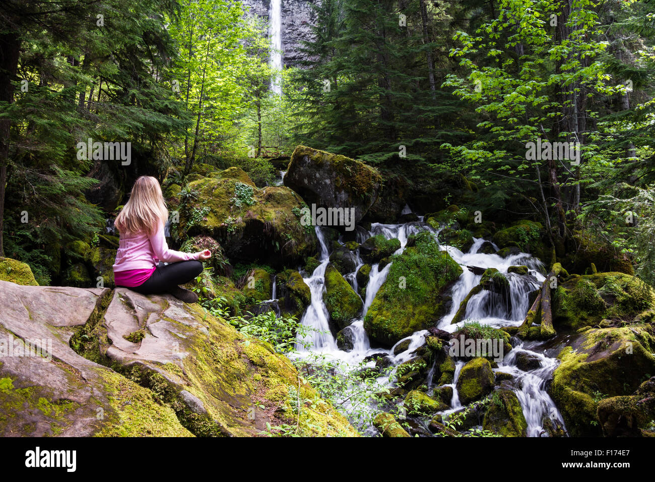 Schöne Frau sitzt auf einem Felsblock Naturbeobachtung mit Watson fällt im Hintergrund Stockfoto