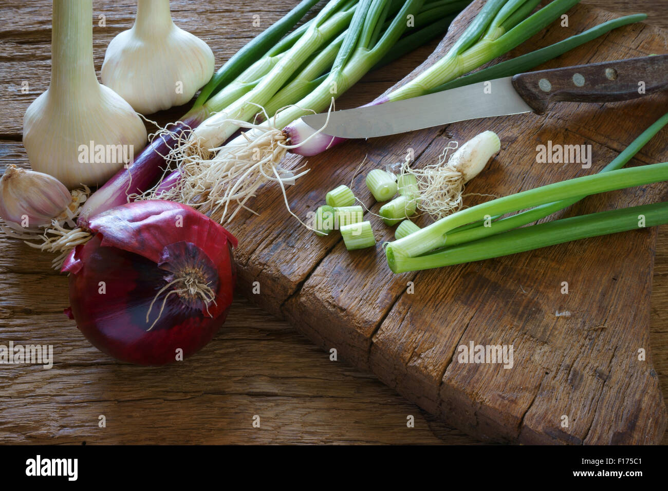 Frische rote Frühlingszwiebeln, Knoblauchzwiebel und einem Küchenmesser auf einem alten Holzbrett Stockfoto