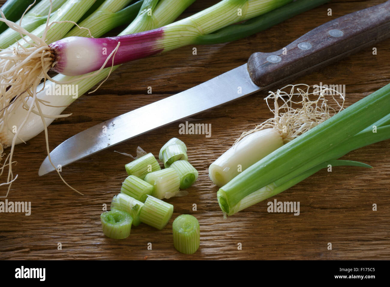 Frische grüne Frühlingszwiebeln mit einem Küchenmesser auf einem alten rustikalen Holzbrett Stockfoto