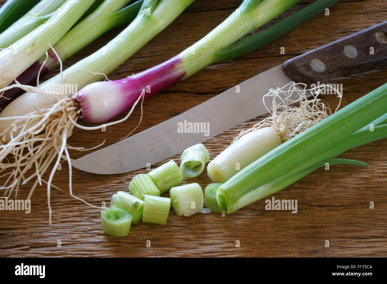Frische grüne Frühlingszwiebeln mit einem Küchenmesser auf einem alten rustikalen Holzbrett Stockfoto