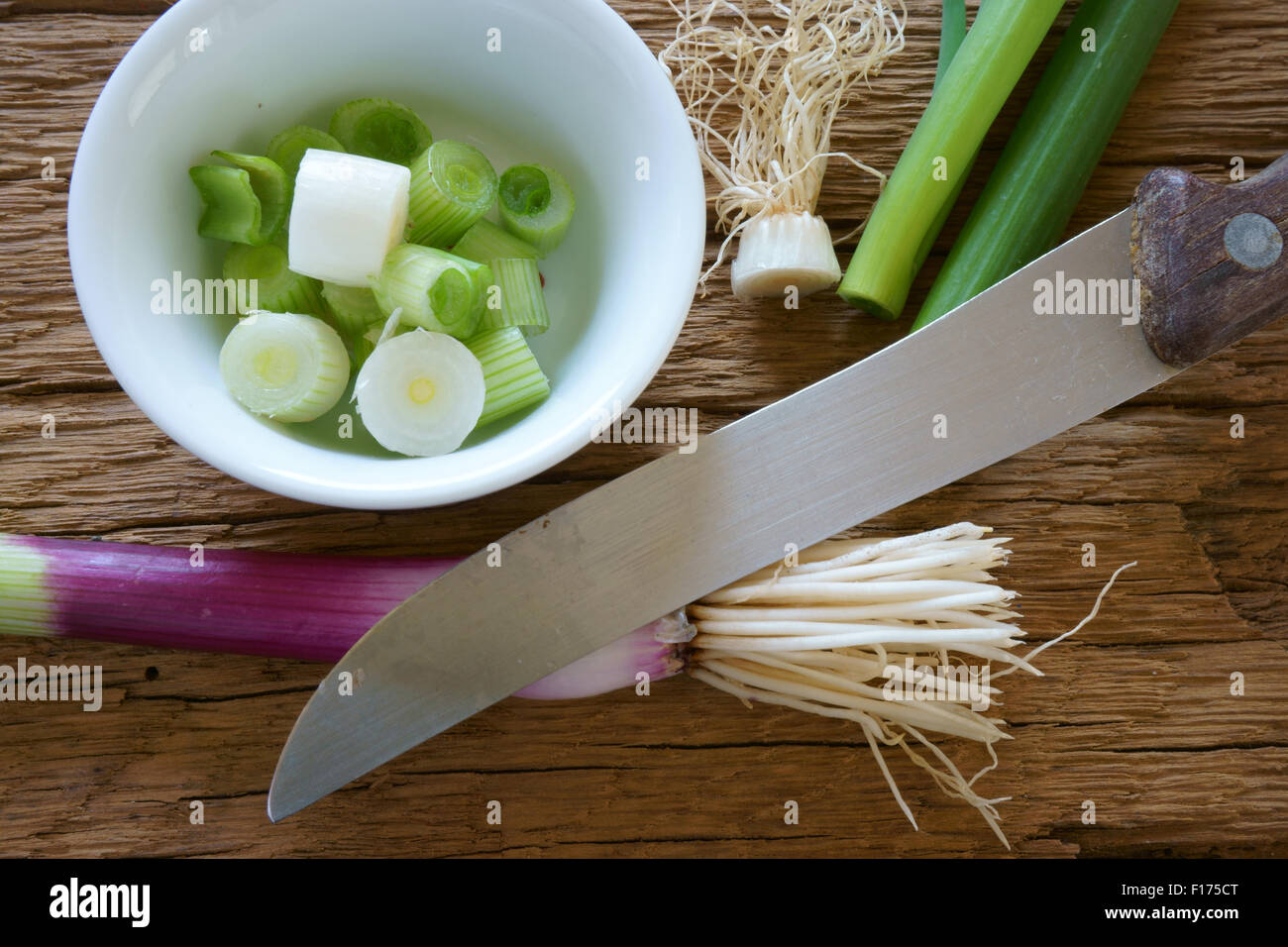 Rote Zwiebeln, eine weiße Porzellanschüssel und einem Küchenmesser auf einem rustikalen Holzbrett Stockfoto