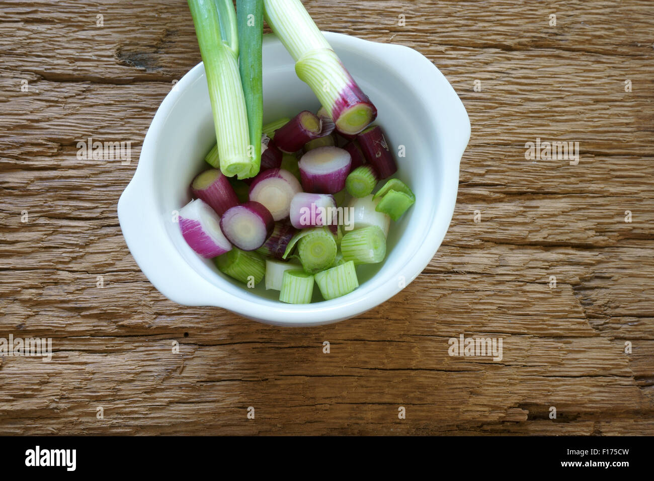 Rot frisch geschnittene Frühlingszwiebeln in eine weiße Porzellanschale auf rustikalem Holzbrett Stockfoto