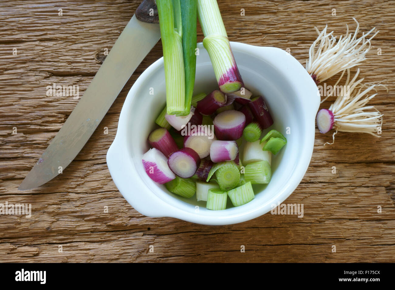 Rot frisch geschnittene Frühlingszwiebeln in eine weiße Porzellanschüssel und ein Messer auf rustikalem Holzbrett Stockfoto