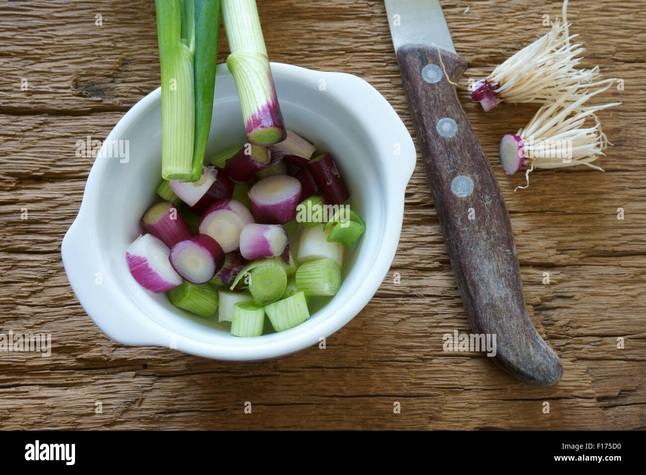 Rot frisch geschnittene Frühlingszwiebeln in eine weiße Porzellanschüssel und ein Messer auf rustikalem Holzbrett Stockfoto
