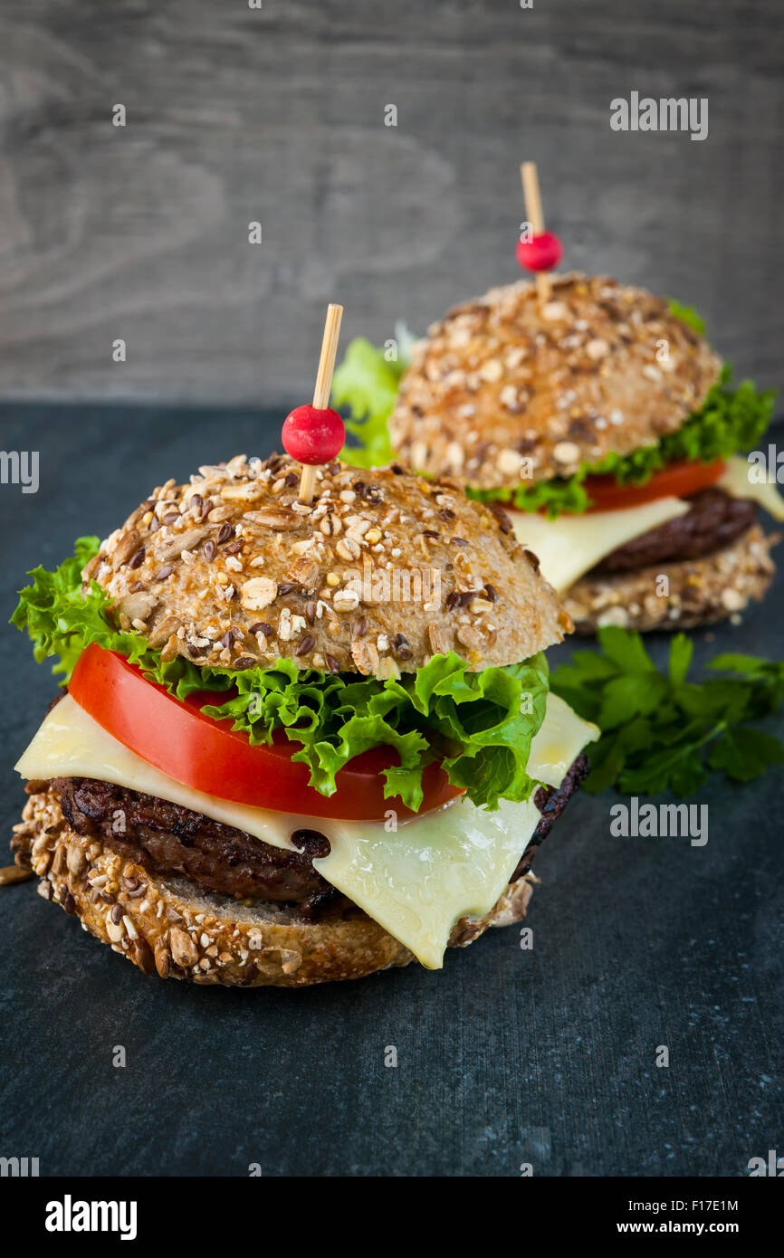 Zwei Gourmet-Hamburger mit Käse und frischem Gemüse auf Mehrkorn Brötchen auf dunklem Hintergrund Stockfoto