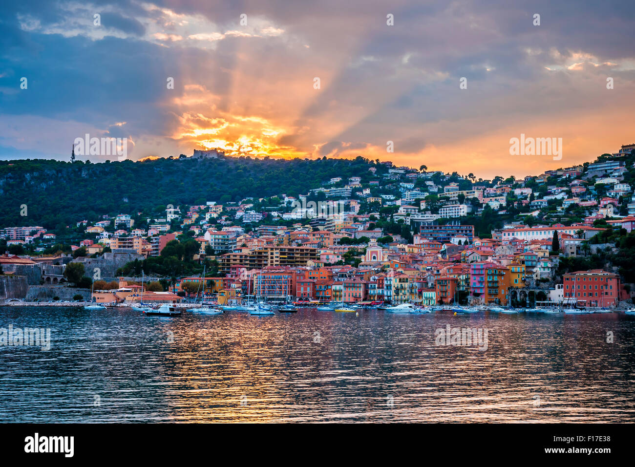 Küstenblick bunte Côte d ' Azur Stadt Villefranche-Sur-Mer am dramatischen Sonnenuntergang mit Sonnenstrahlen reflektieren im Hafen. Stockfoto