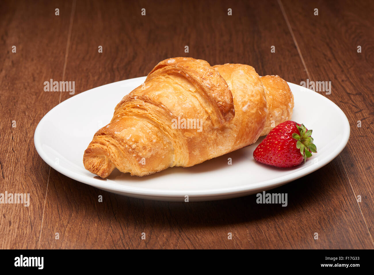 Frische französische Croissants und Erdbeere auf weißen Keramikplatte auf dunklen Holztisch Hintergrund Stockfoto