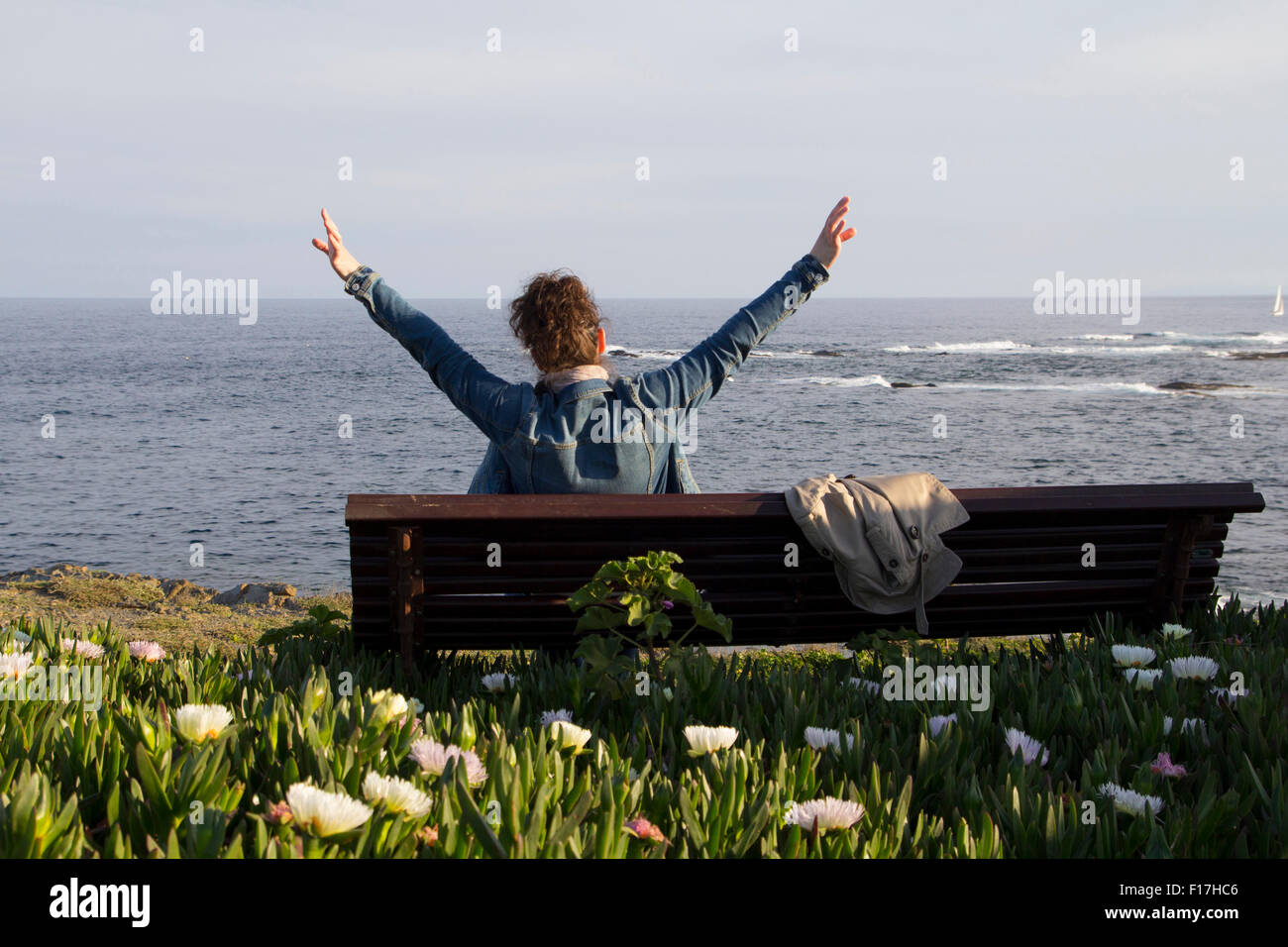 Frau sitzt direkt am Meer, mit offenen Armen Stockfoto