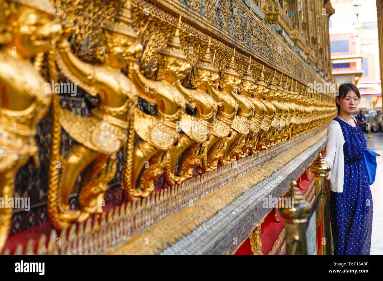 Ein Tourist posiert für ein Foto vor mythologischen garuda- und Nagagaskulpturen im Wat Phra Kaew im Grand Palace Complex in Bangkok, Thailand. Stockfoto