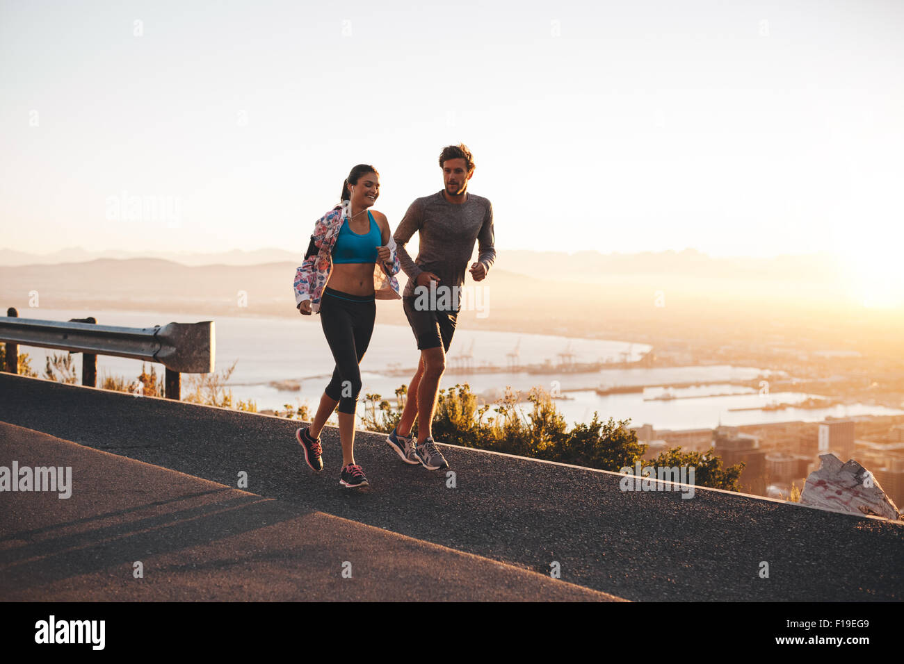 Junges Paar in frühen Morgenstunden Joggen. Junger Mann und Frau im Freien auf einer Hügel-Straße laufen. Stockfoto