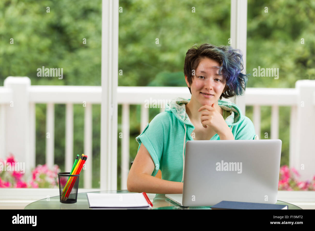 Lächelnde Teenager-Mädchen, ich freue mich, mit Computer, Bücher und Stifte im Vordergrund. Große Fenster im Hintergrund verschwommen Stockfoto