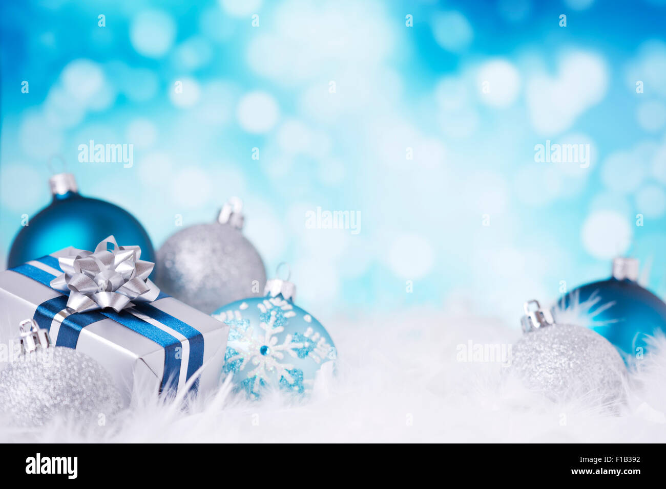 Blau und Silber Weihnachtskugeln und ein Geschenk auf eine weiche federleichte Oberfläche vor defokussierten blaue und weiße Lichter. Stockfoto