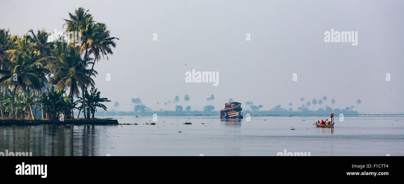 Ruhig am frühen Morgen Wasser des Vembanad See, Kumarakom in den Backwaters von Kerala. Boote und Palmen, die in Ferne sichtbar Stockfoto