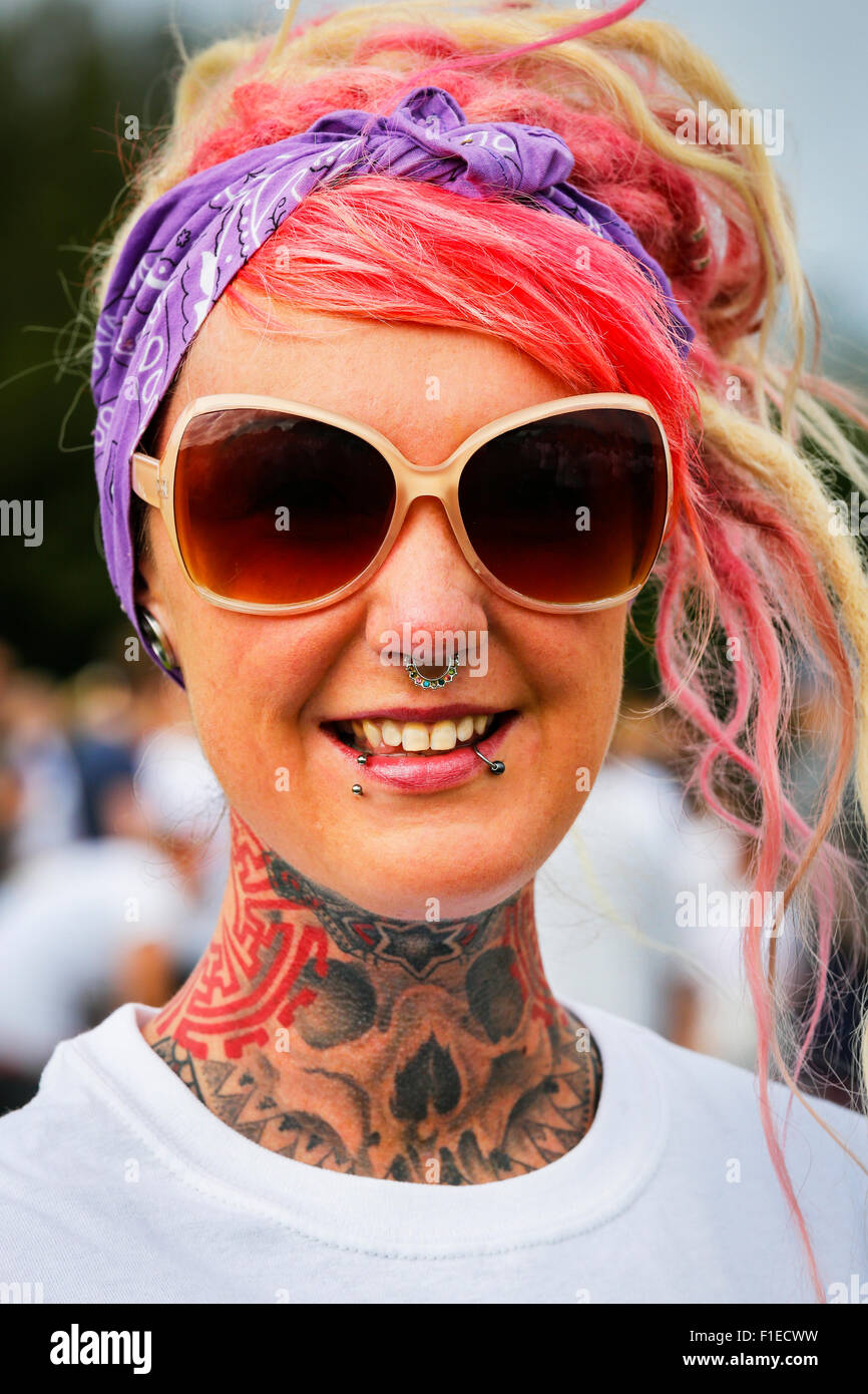 Junge Frau mit einem vollen Hals Tattoo, Gesichts-Piercings und Nieten und gefärbten roten Haaren. Stockfoto