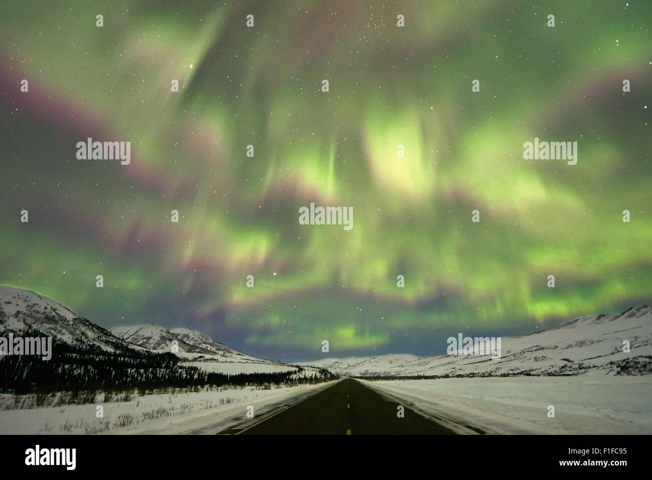 Schimmernde Nordlicht am Himmel über der Straße und Gebirgsketten in Alaska Stockfoto