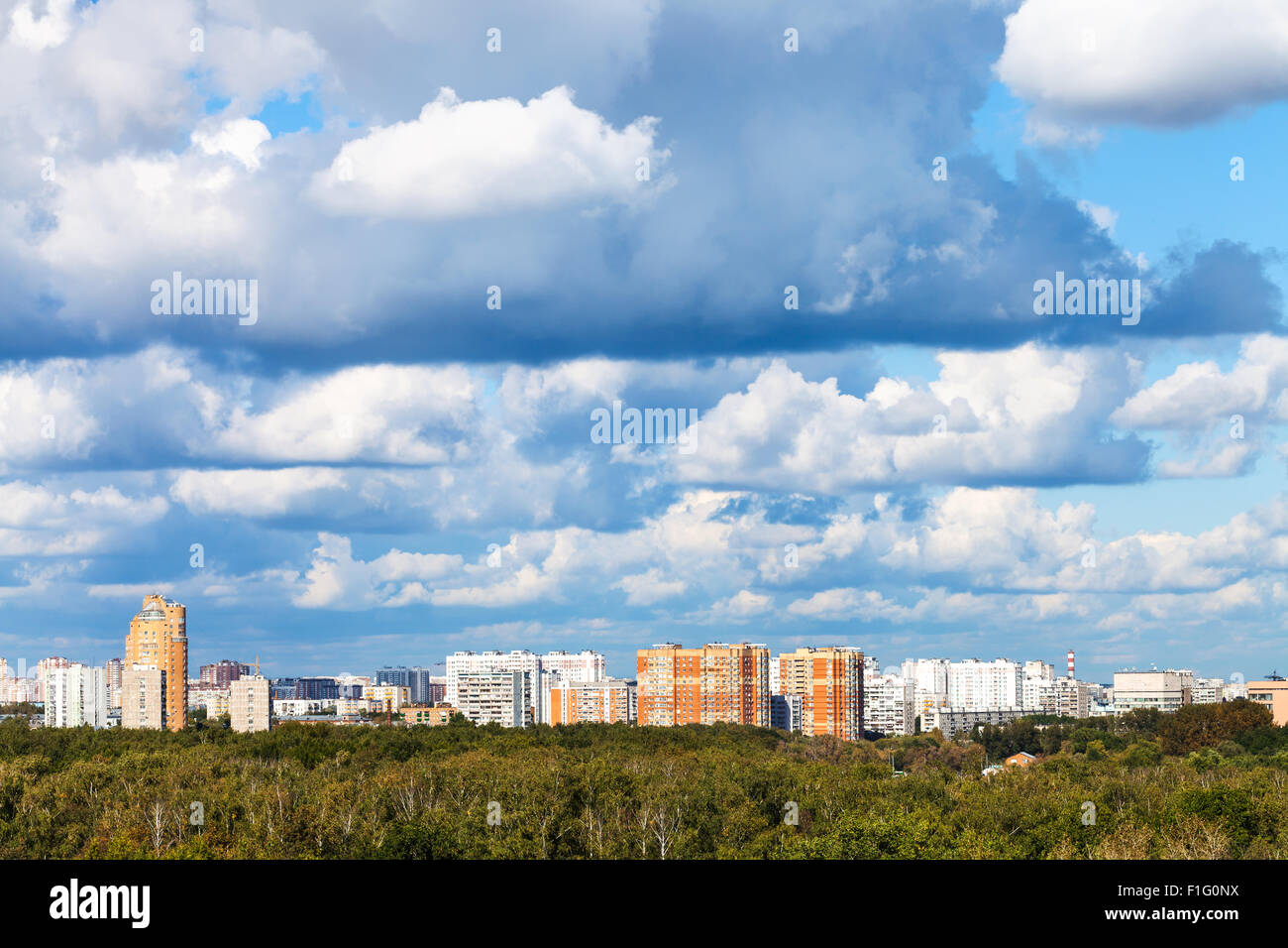 niedrige blaue Wolken über grünen Wald und Stadt im Sommer Stockfoto