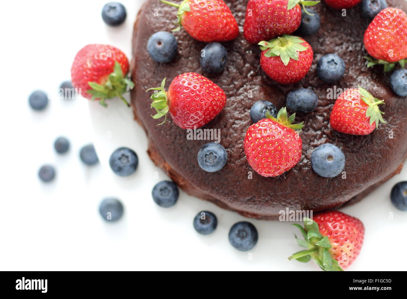 Nahaufnahme von Schokoladenkuchen mit Beeren an der Spitze vor weißem Hintergrund Stockfoto