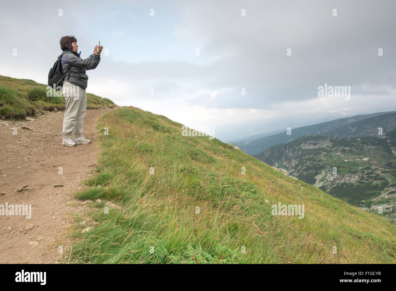 Ältere Frau fotografieren mit Smartphone auf dem Berg. Dramatischer Himmel Stockfoto
