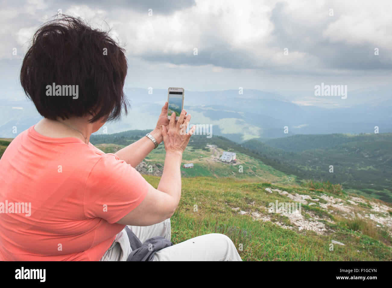 Ältere Frau fotografieren mit Smartphone auf dem Berg. Dramatischer Himmel Stockfoto