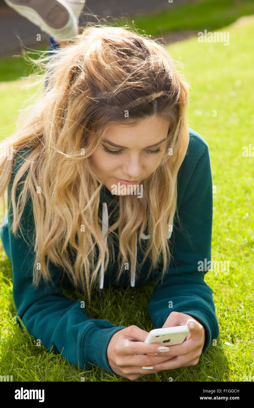Ziemlich junges Mädchen liegend auf dem Rasen ein Mobiltelefon in ihren Händen hält. Stockfoto