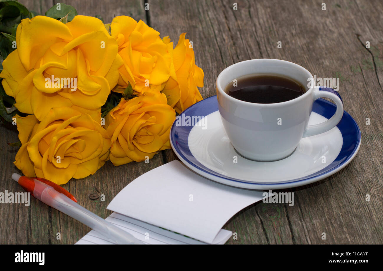 Notebook mit Griff, Kaffee und einem Bouquet von leuchtend gelben Rosen Stockfoto