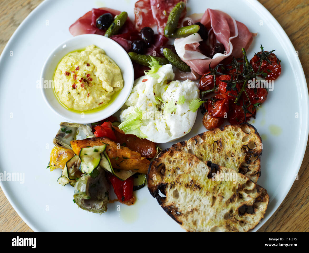 Eine Auswahl an Schinken und Gemüse, serviert mit Sauce und Brot auf einem weißen Teller. Stockfoto