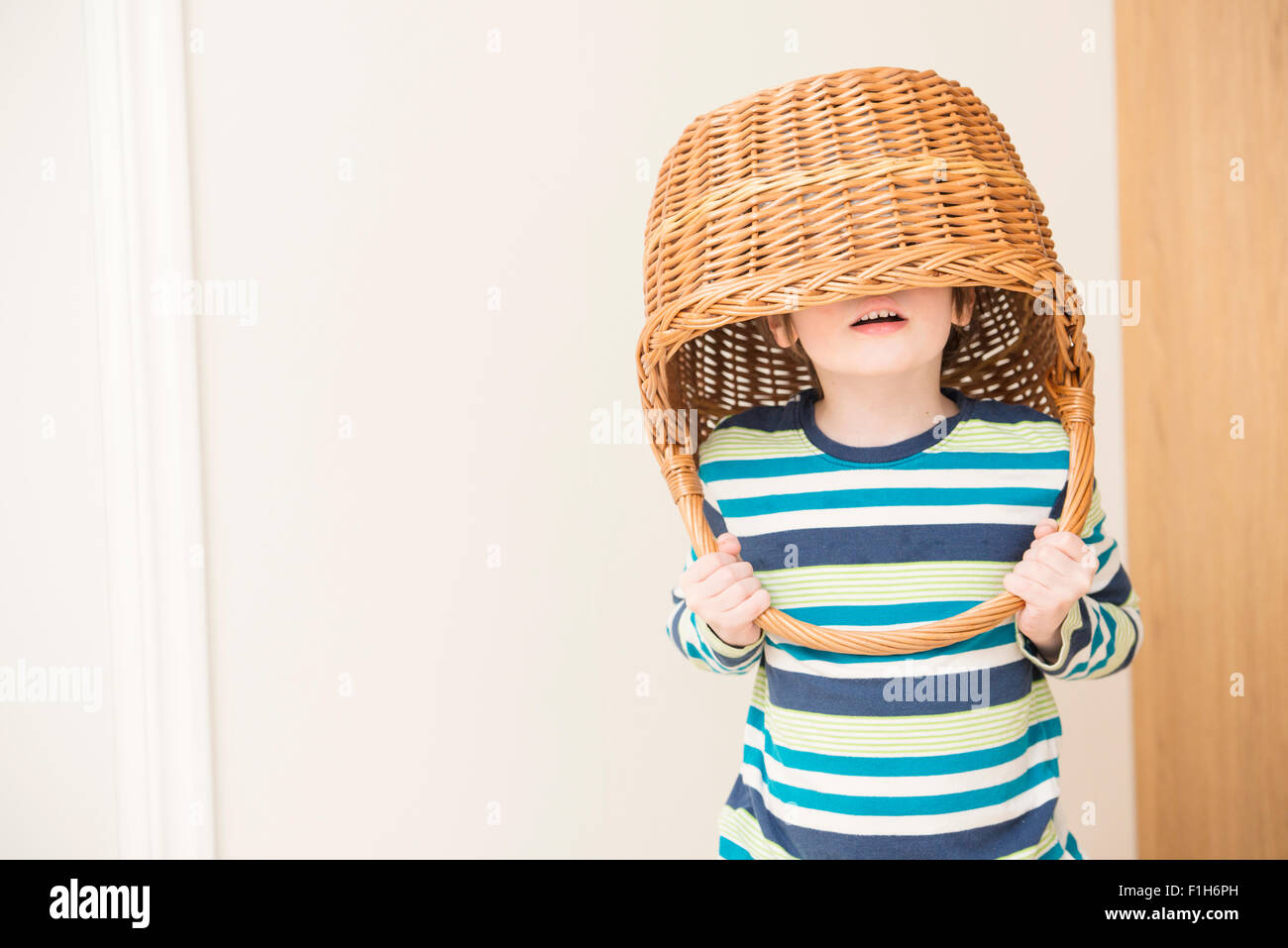 Kleine Mädchen spielen und Weidenkorb über ihren Kopf halten. Konzeptbild von Kindheit Spaß, Fantasie und Vorstellungskraft. Stockfoto