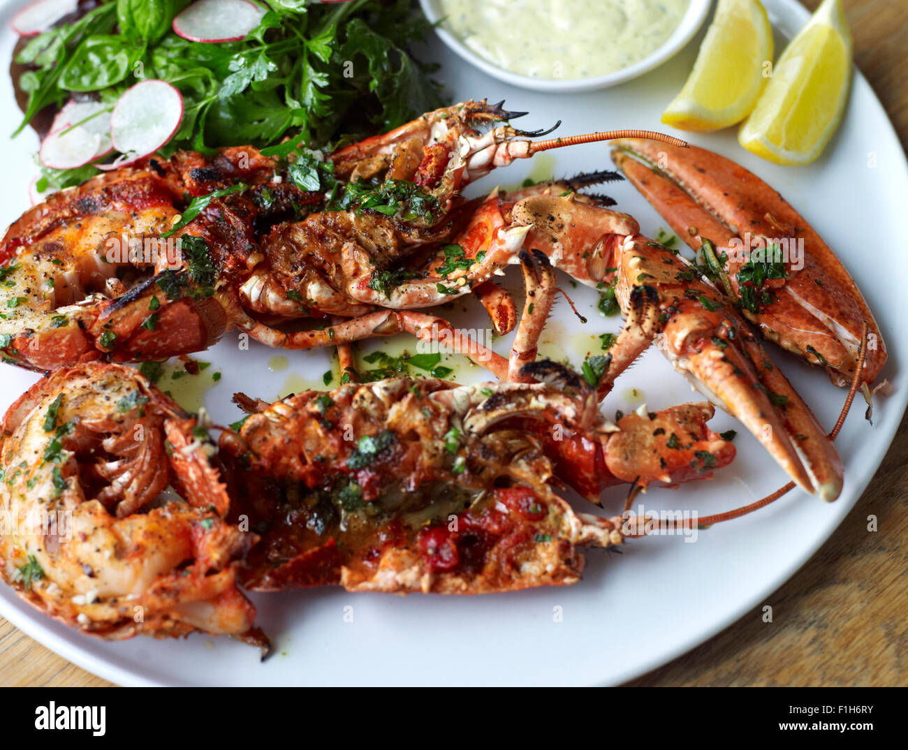 Eine Nahaufnahme von Hummer und Schalentiere präsentiert auf einem Teller mit Zitrone, Remoulade, Würze und einen Salat. Stockfoto