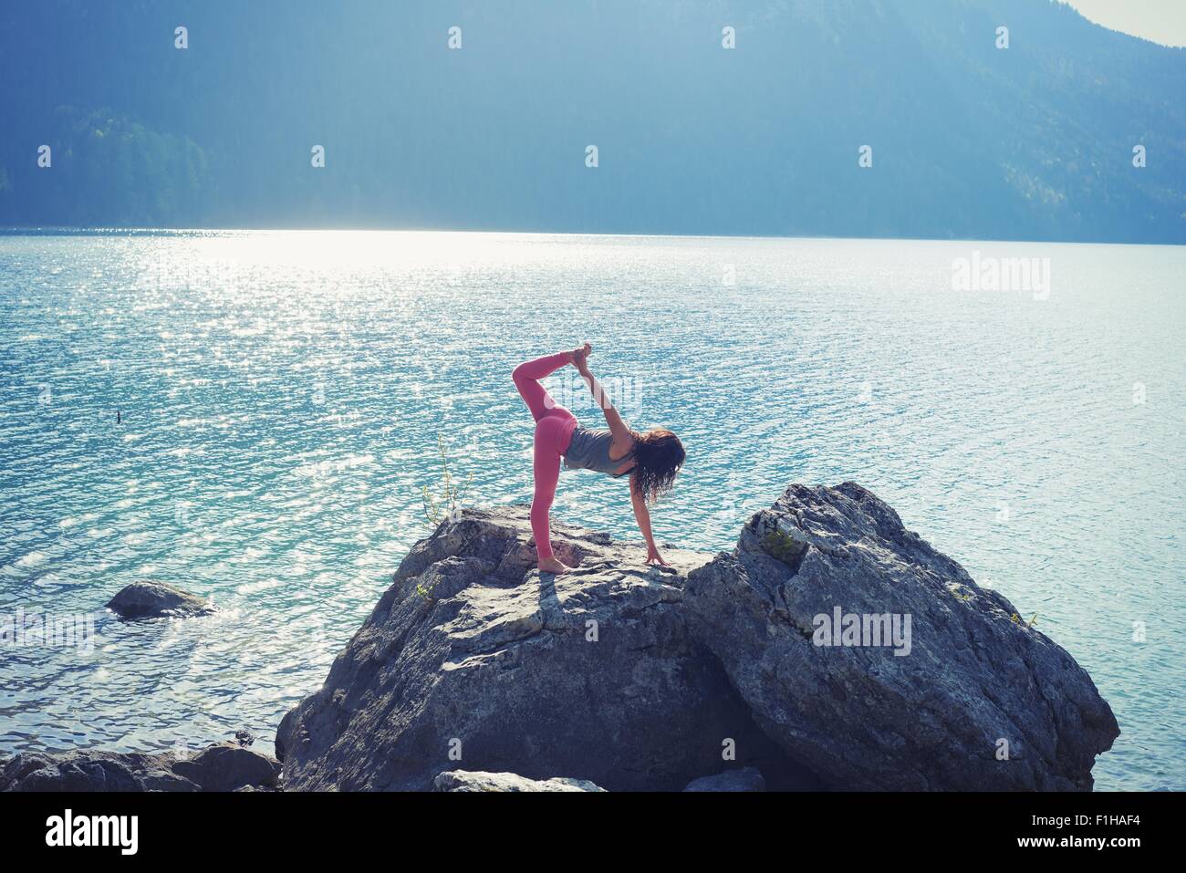 Mitte Erwachsene Frau, balancieren auf Rock am See in Yogaposition Stockfoto