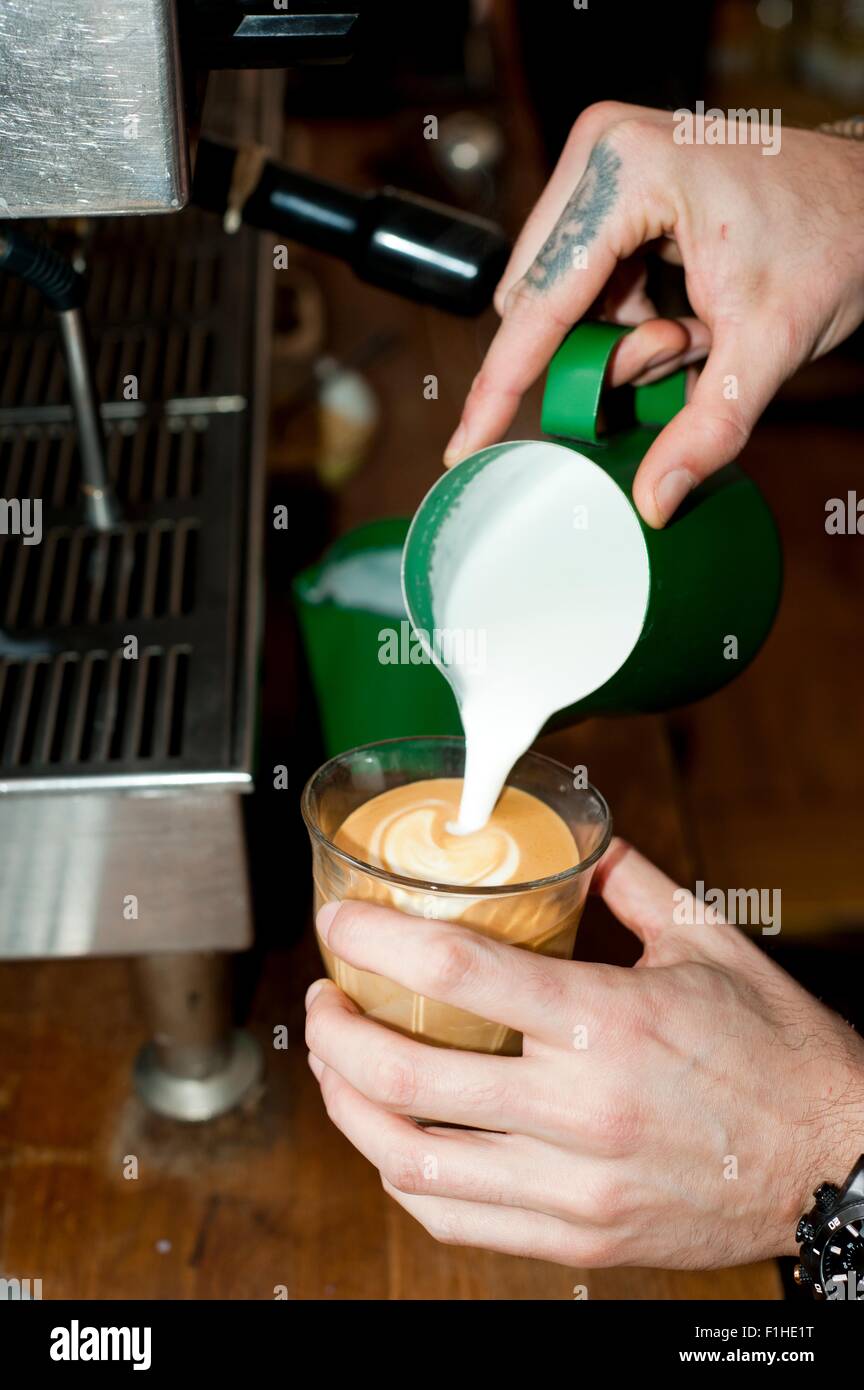 Hände des Café Kellner gießt Milchschaum in Latte Glas Stockfoto